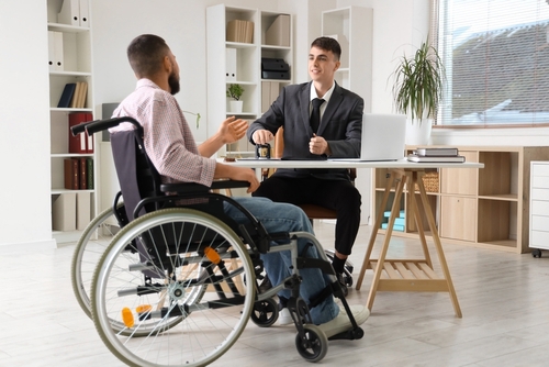 suited attorney meeting with wheelchair-using client across office desk with laptop