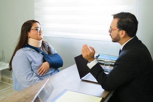 Client wearing neck brace and arm sling meeting with attorney across desk